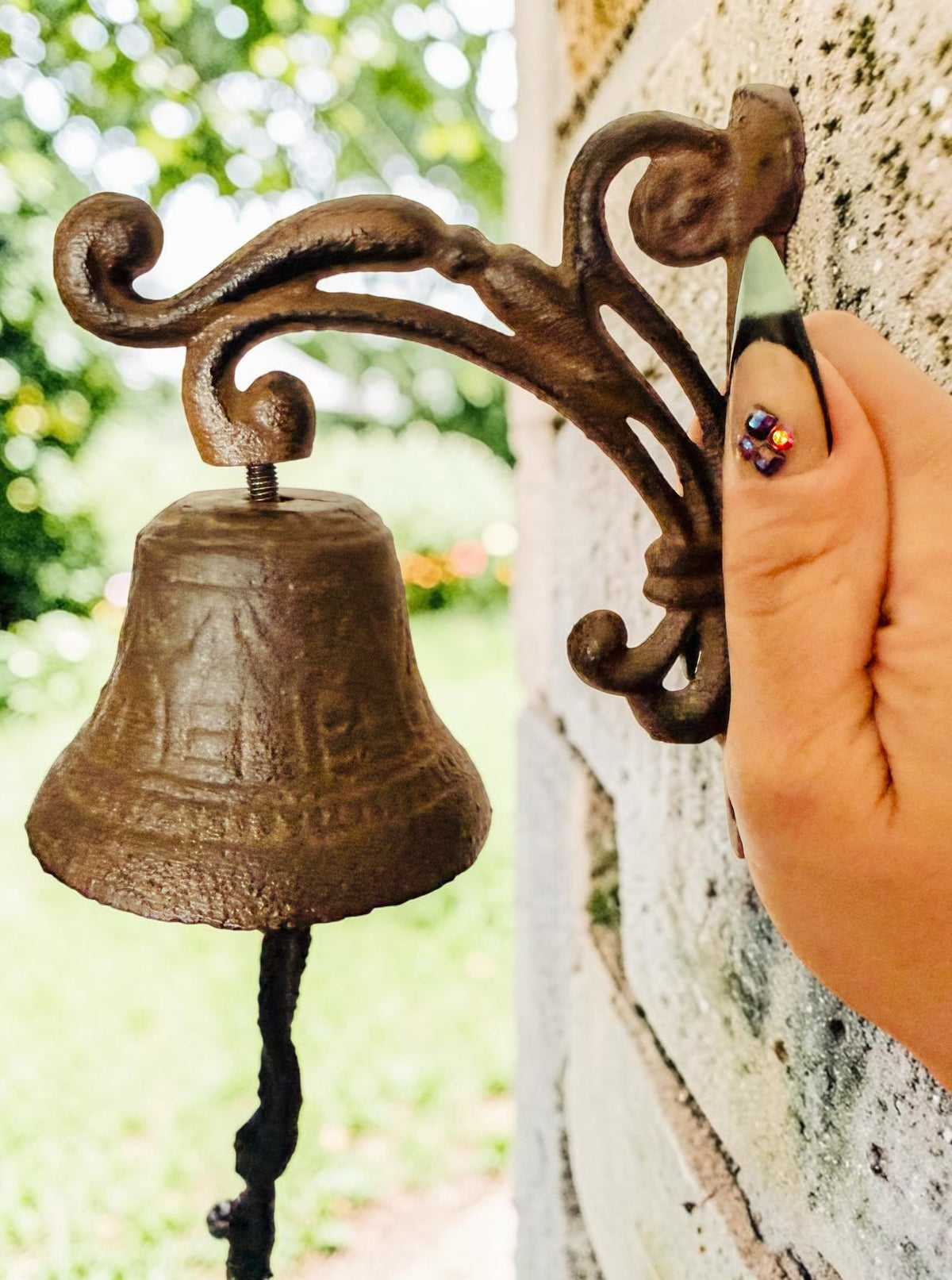 Chica Mexico cast iron wall-mounted bell with ornate scrolled bracket and rope pull on a stone wall